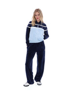 Woman wearing a navy tracksuit with a light blue panel on a white background