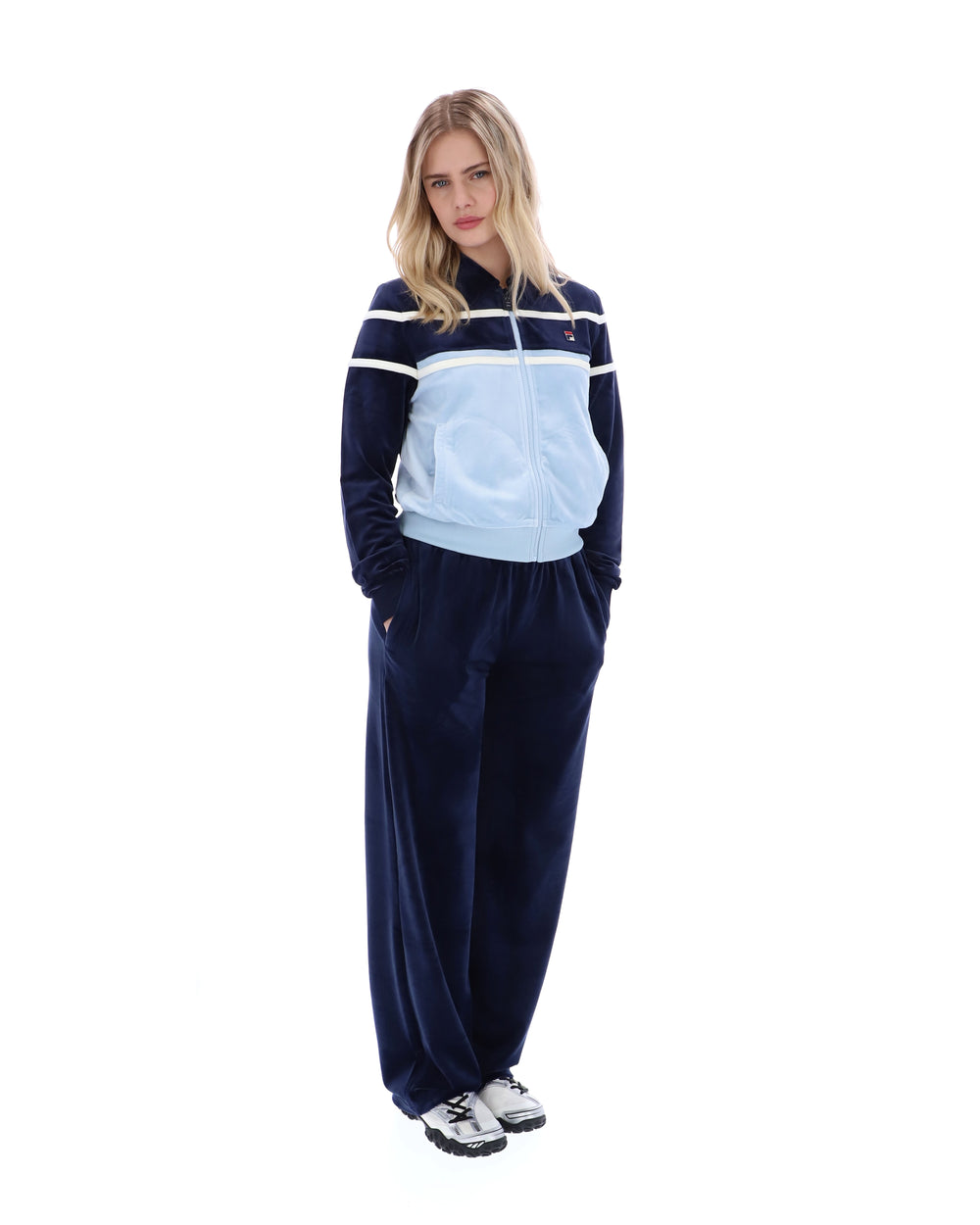 Woman wearing a navy tracksuit with a light blue top on a white background