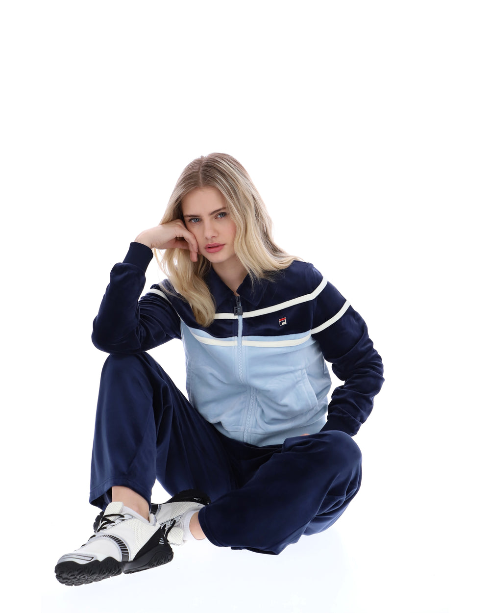 Woman wearing a navy tracksuit with a light blue panel on a white background