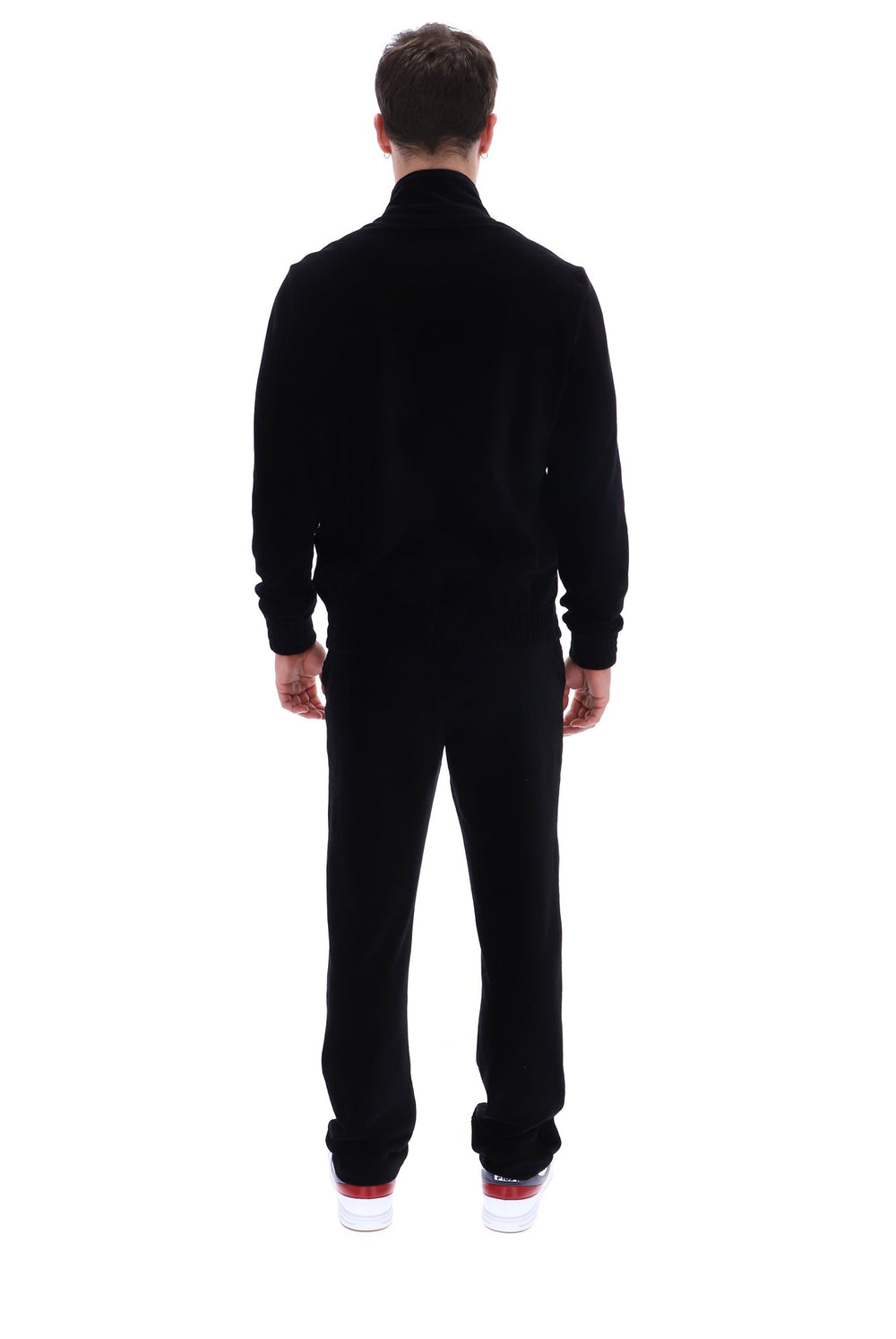 A man viewed from behind wearing a black long-sleeve mock-neck fleece jacket and matching black fleece pants, paired with white sneakers with red soles, against a solid white background.