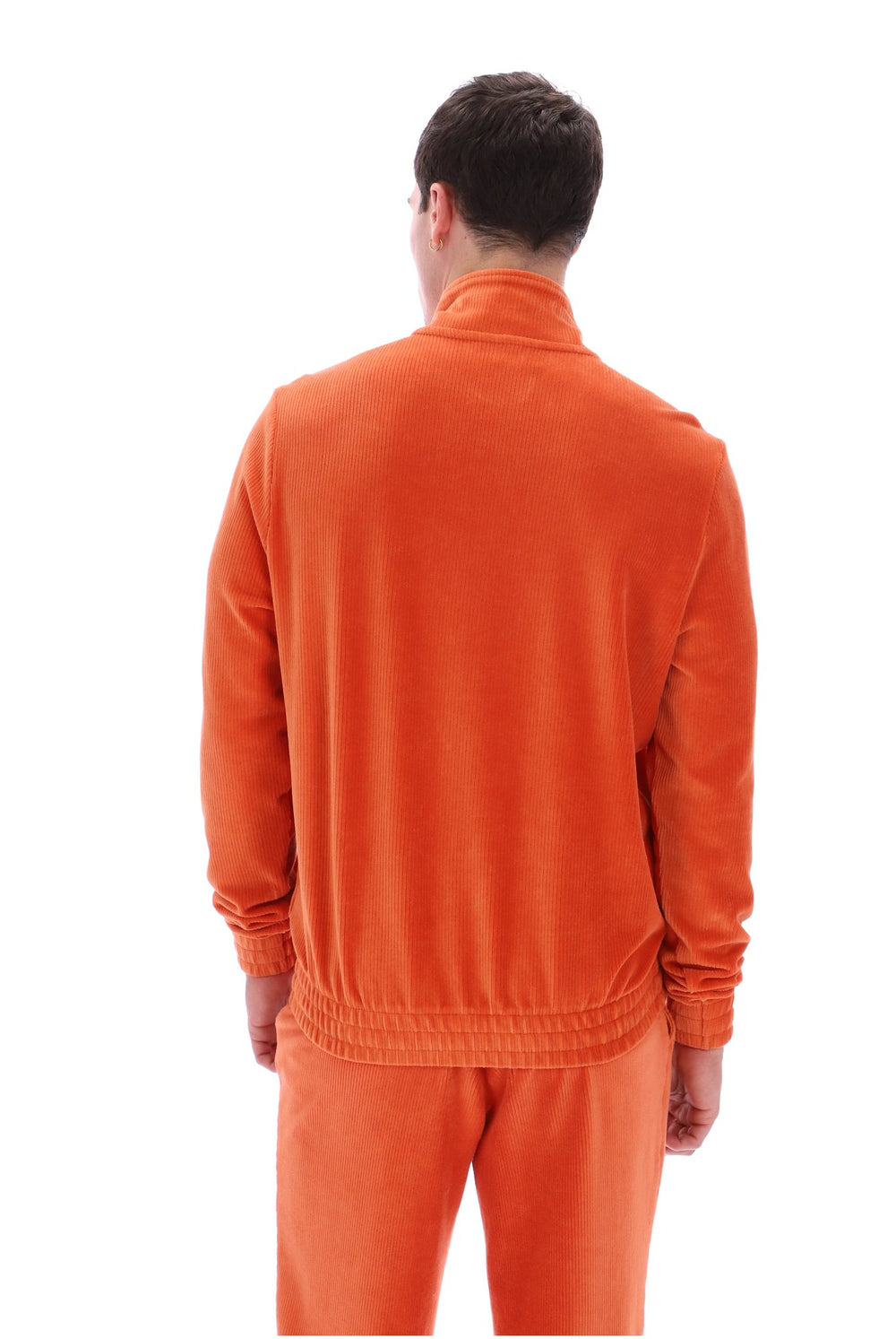 A man viewed from the back wearing an orange long-sleeve zip-up jacket and matching orange pants against a plain white background.