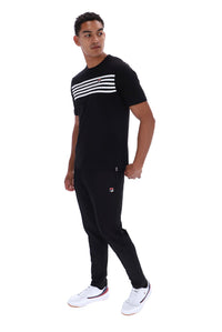 A man modeling a black short-sleeve t-shirt with three white horizontal stripes across the chest, paired with black joggers featuring a small red and white logo on the left thigh, and white sneakers, set against a plain white background.
