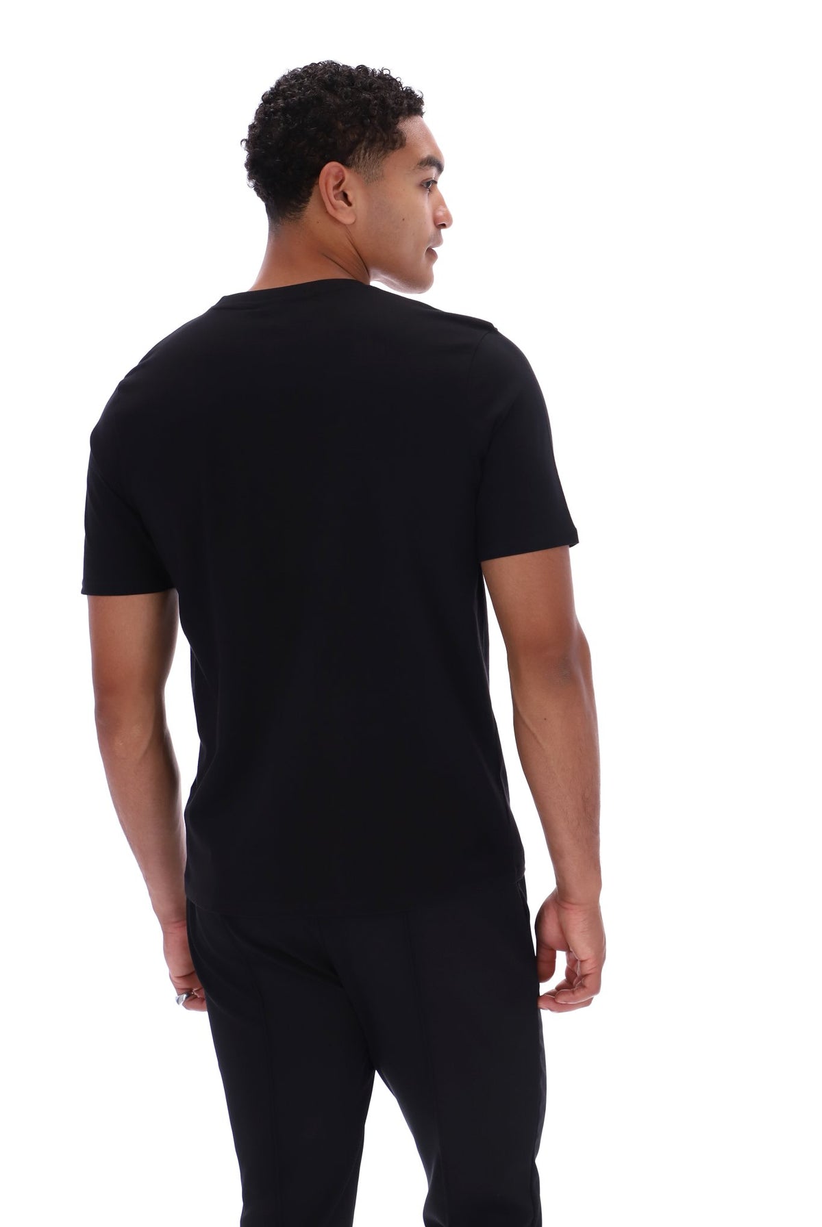 A man wearing a plain black short-sleeve t-shirt and black pants, photographed from the back against a solid white background.