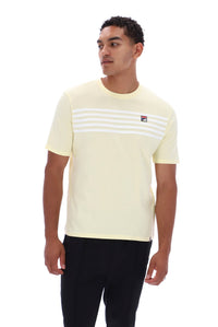 A man wearing a pale yellow short-sleeve t-shirt with white horizontal stripes across the chest and a small Fila logo on the left chest, paired with black pants, against a plain white background.