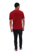 A man viewed from behind wearing a red short-sleeve t-shirt, black pants, and white sneakers with red and blue accents, set against a plain white background.