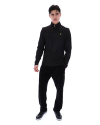 Man wearing a black jacket with a FILA gold logo, paired with matching bottoms, against a white background
