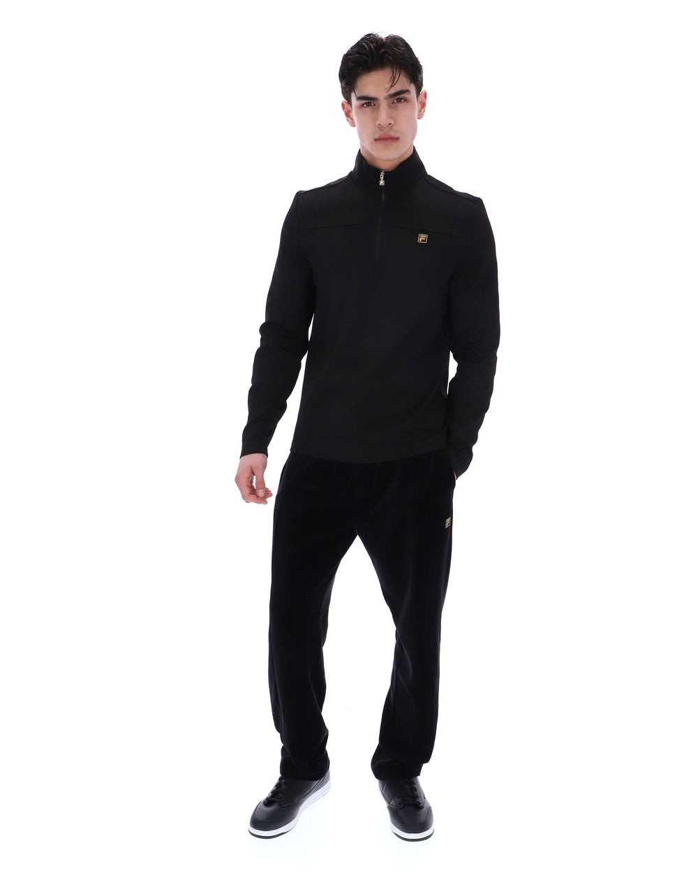 Man wearing a black jacket with a FILA gold logo, paired with matching bottoms, against a white background