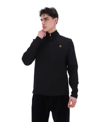 Man wearing a black jacket with a FILA gold logo, paired with matching bottoms, against a white background