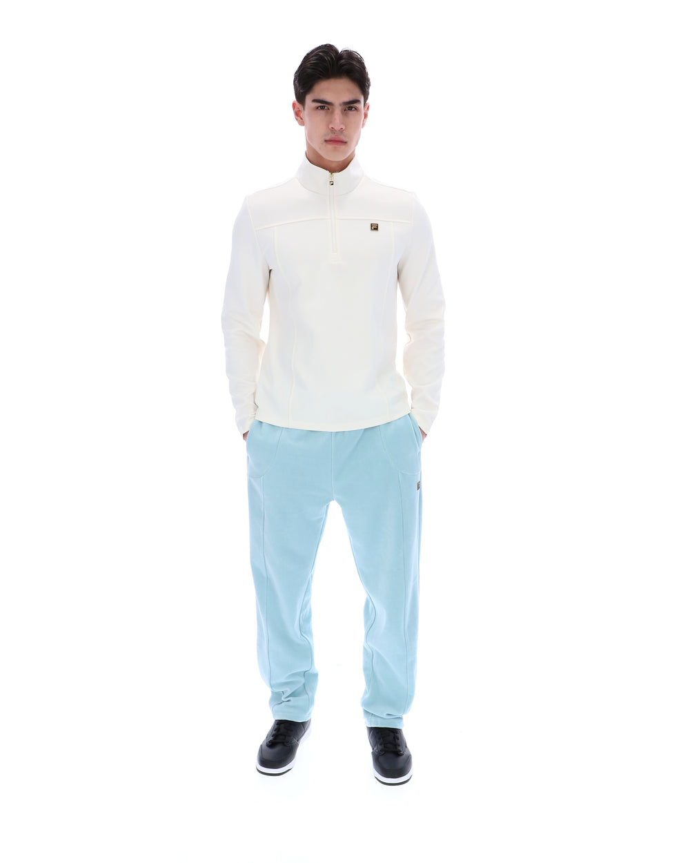 Person wearing a white quarter zip jumper and light blue pants on a white background