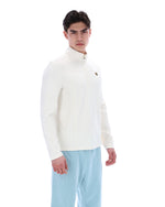 Man wearing a white quarter zip jumper and light blue pants on a white background
