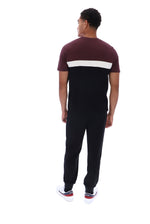 A man viewed from behind wearing a short-sleeve t-shirt with a maroon upper section, a white horizontal stripe across the back, and black pants, paired with white sneakers.