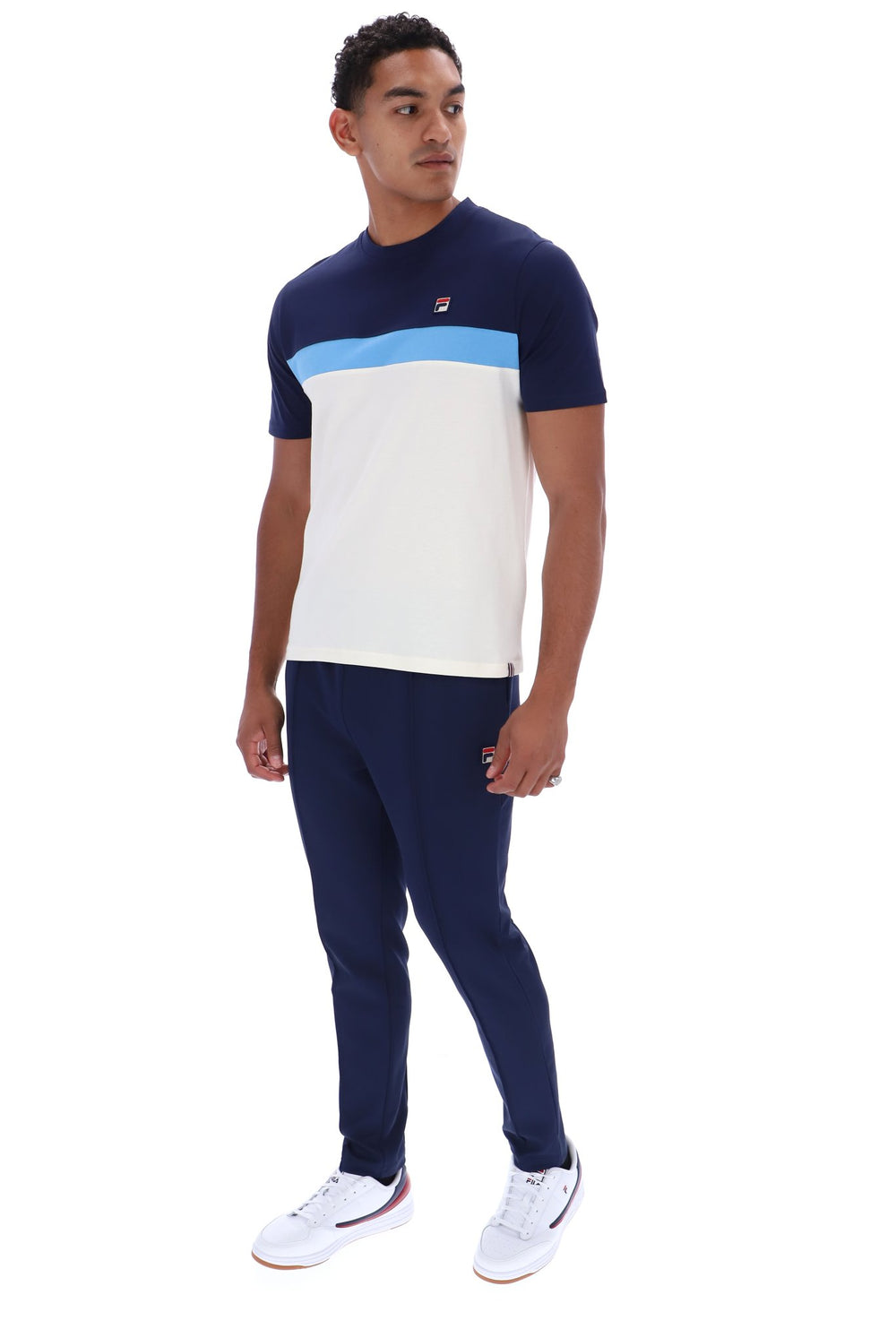 A man modeling a short-sleeve athletic t-shirt and matching jogger pants set. The t-shirt features a navy blue upper chest and shoulders, a light blue horizontal stripe, and a large white lower body.