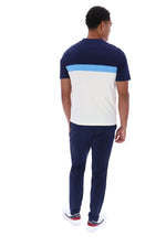 A man viewed from behind wearing a short-sleeve colorblock t-shirt with navy blue, light blue, and white blocks, paired with navy pants and white sneakers.