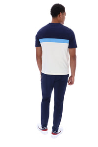 A man viewed from behind wearing a short-sleeve colorblock t-shirt with navy blue, light blue, and white blocks, paired with navy pants and white sneakers.