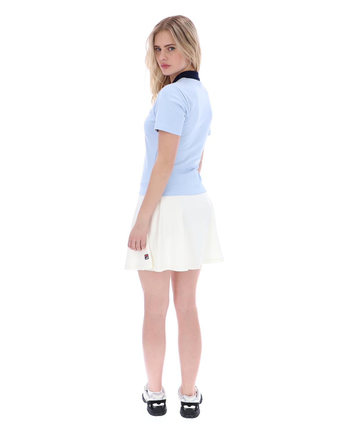 Woman wearing a light blue polo shirt and white skirt on a white background