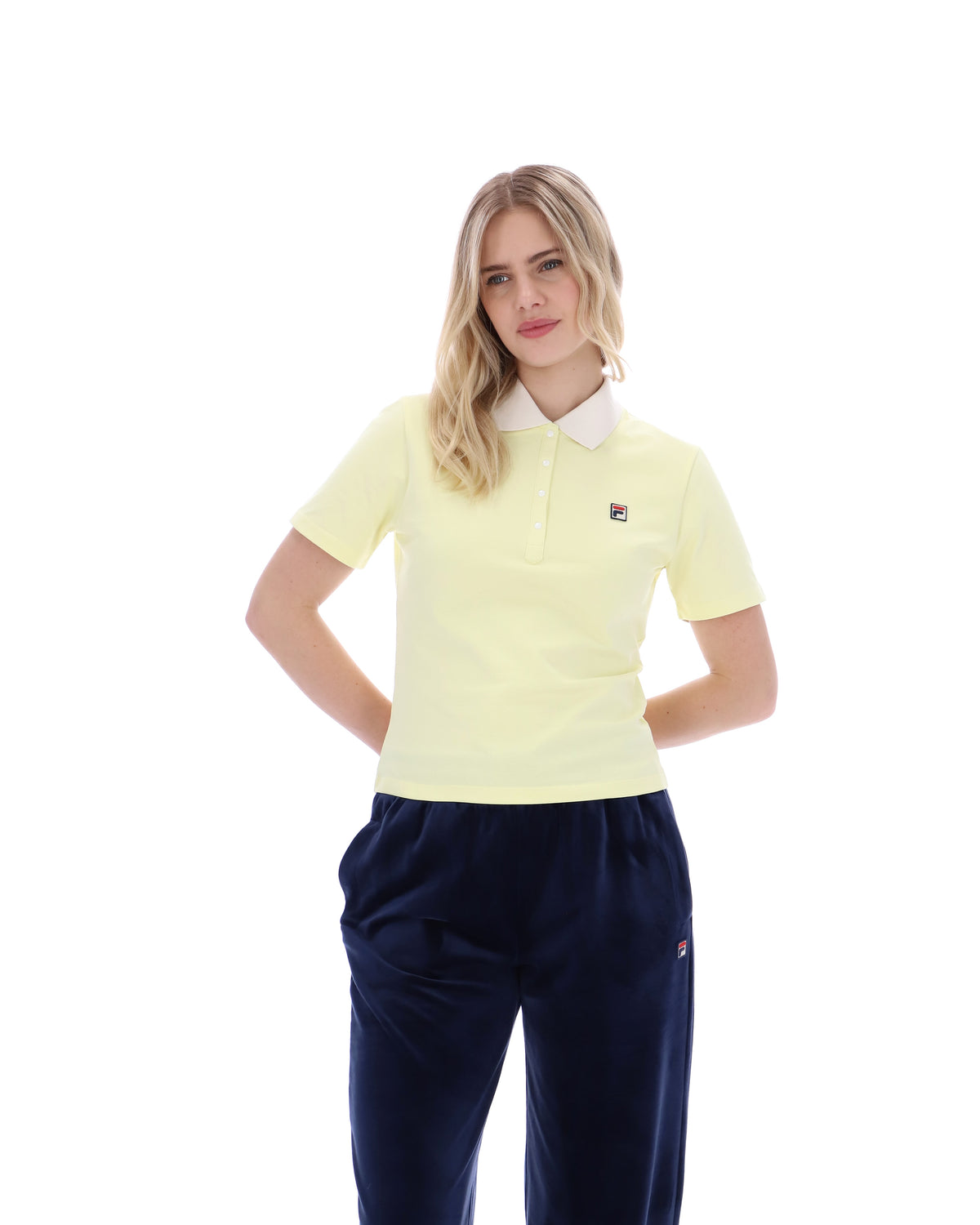 Woman wearing a light yellow polo shirt and navy pants on a white background