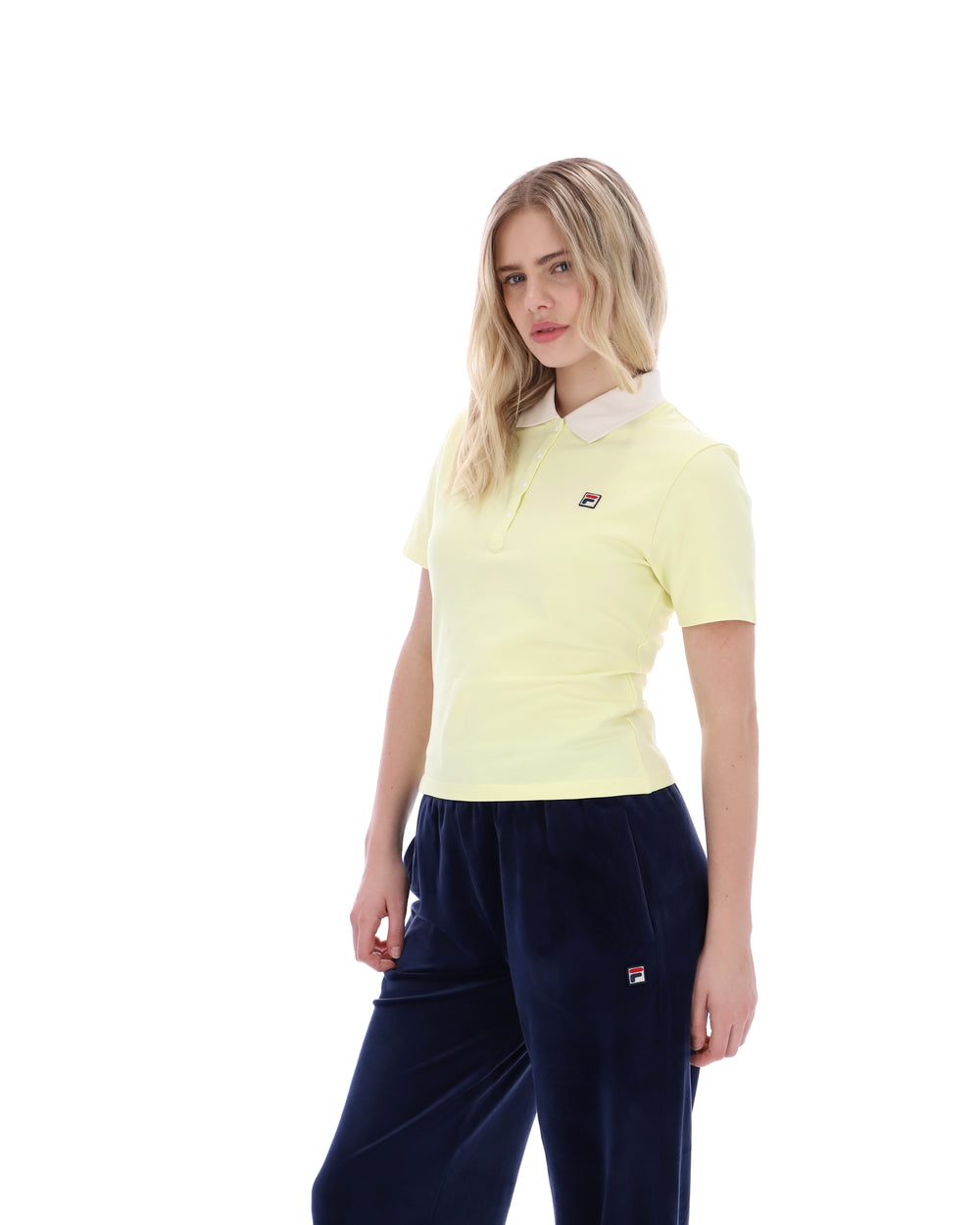 Woman wearing a light yellow polo shirt and navy pants on a white background