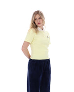 Woman wearing a light yellow polo shirt and navy pants on a white background