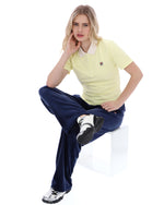Woman sitting on a white stool wearing a yellow shirt and navy pants.