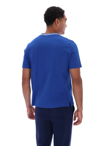 A man viewed from the back wearing a royal blue short-sleeve crewneck t-shirt and navy blue pants, set against a plain white background.