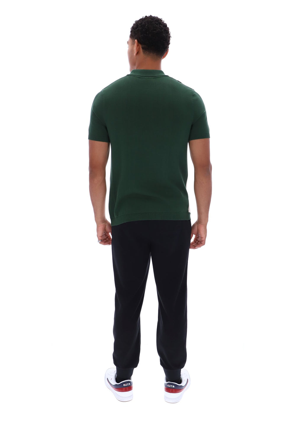 A man viewed from behind wearing a dark green short-sleeve polo shirt, black pants, and white sneakers with red accents, set against a plain white background.