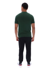 A man viewed from behind wearing a dark green short-sleeve polo shirt, black pants, and white sneakers with red accents, set against a plain white background.