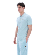 A man wearing a light blue zip-up polo shirt with a FILA gold logo on the chest, on a white background
