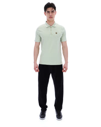 Man wearing a light green polo shirt and black pants on a white background