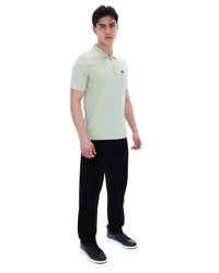 Man wearing a light green polo shirt and black pants on a white background