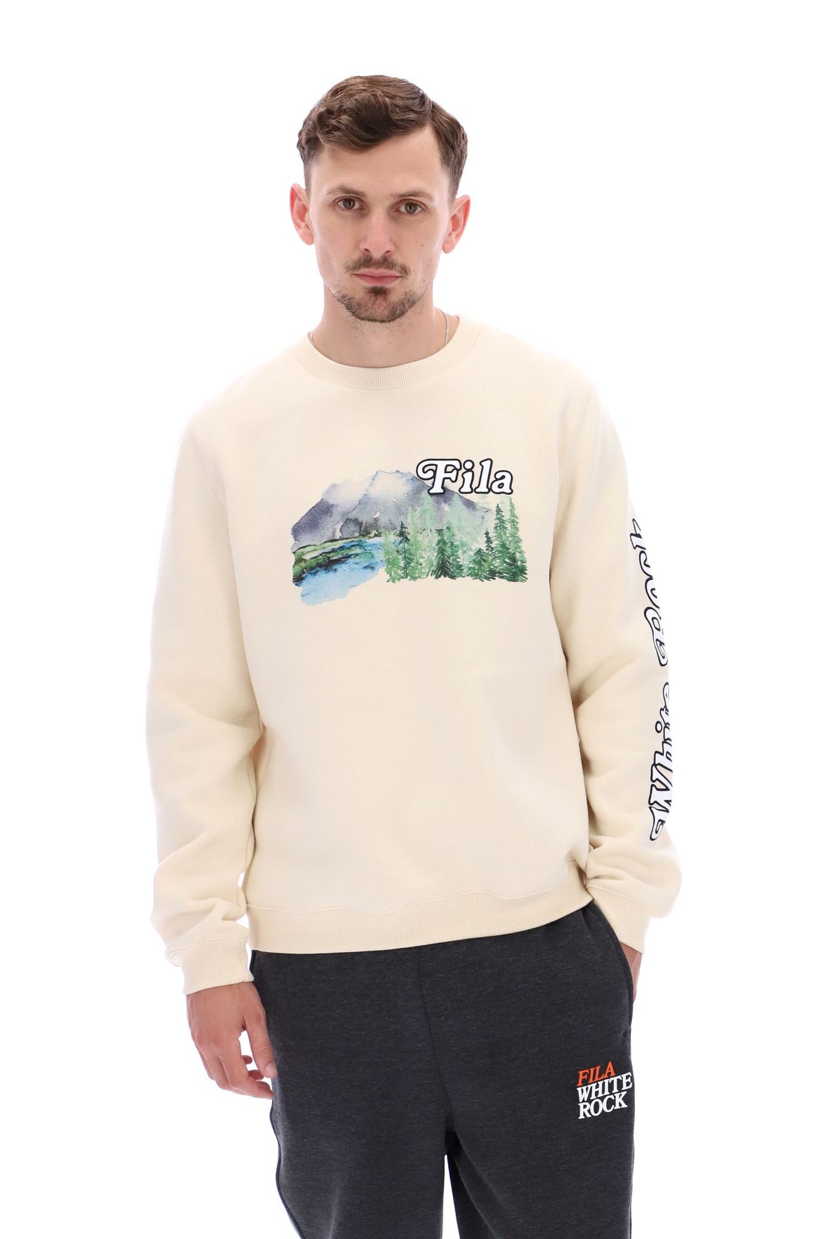 A male model wearing a beige FILA Len Graphic Crew Sweatshirt with a mountain range and brand logo on the front.