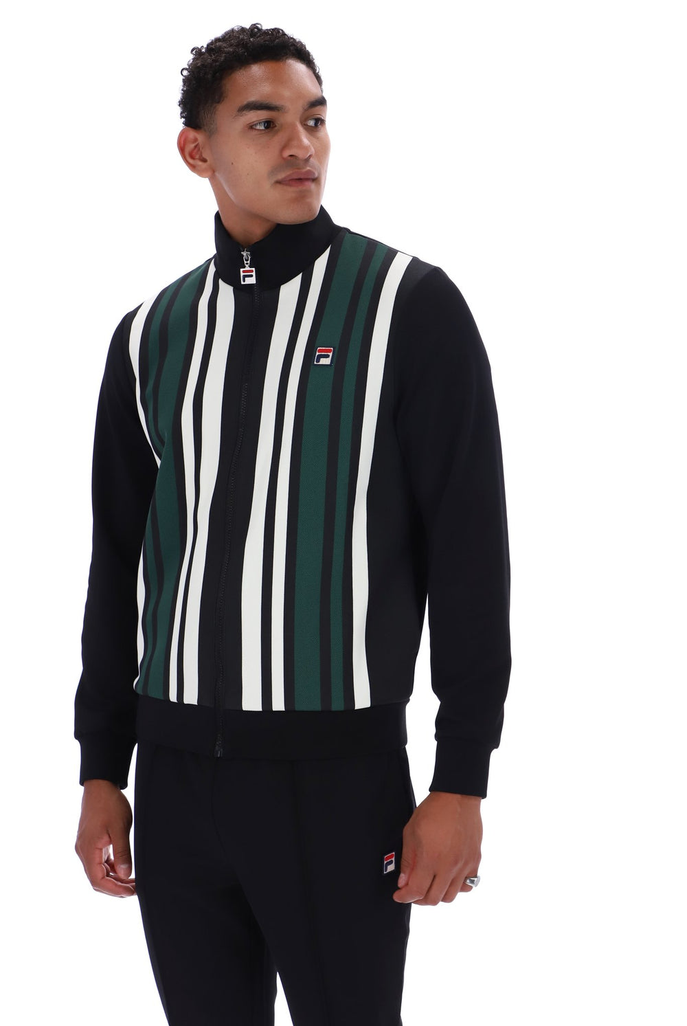 A man wearing a black quarter-zip sweatshirt with vertical green and white stripes on the front, paired with black track pants, against a plain white background.