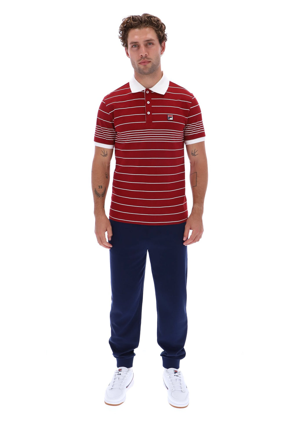 A man modeling a red and white striped short-sleeve polo shirt with a white collar, paired with navy blue jogger pants and white sneakers, against a plain white background.