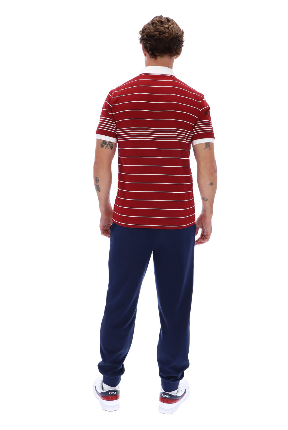 A man viewed from behind wearing a red short-sleeve t-shirt with thin white horizontal stripes, navy blue sweatpants, and white sneakers with red and navy accents, set against a plain white background.