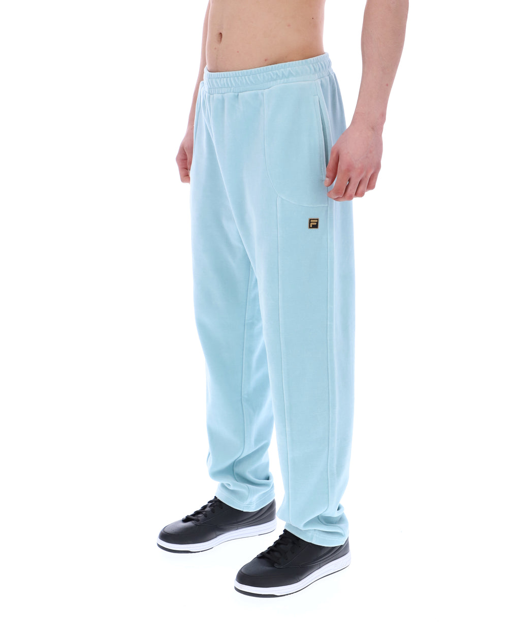 Light blue velour sweatpants with a small FILA logo, worn by a person against a white background