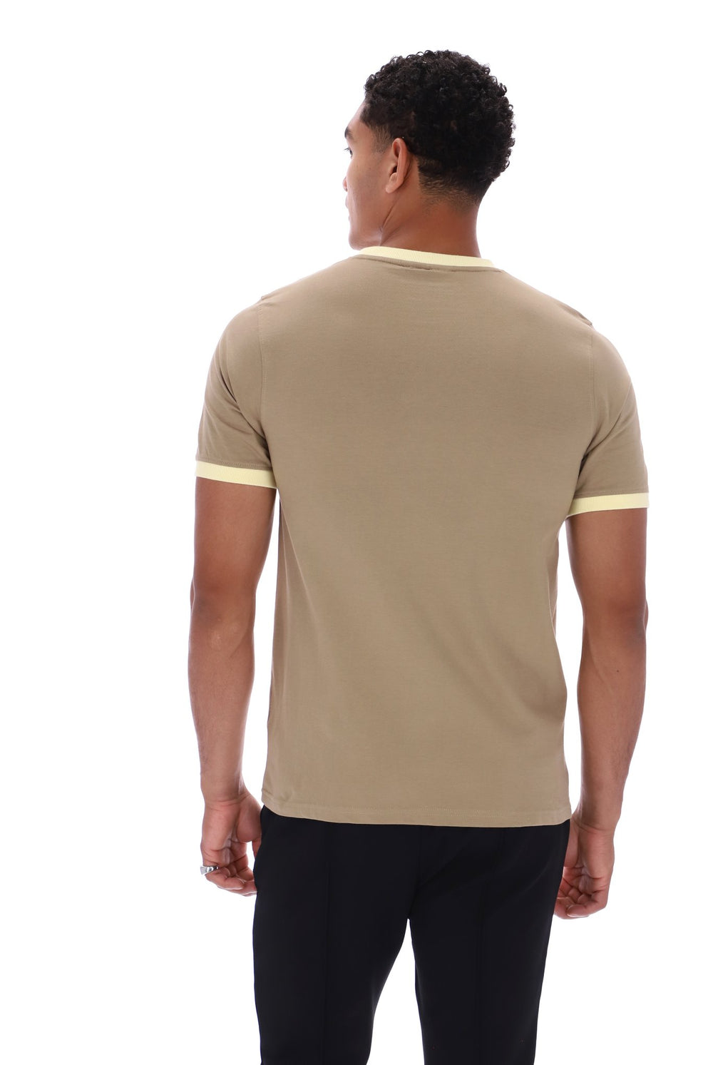 A man viewed from the back wearing a beige short-sleeve t-shirt with light yellow contrast trim at the collar and sleeve cuffs, paired with black pants, against a plain white background.