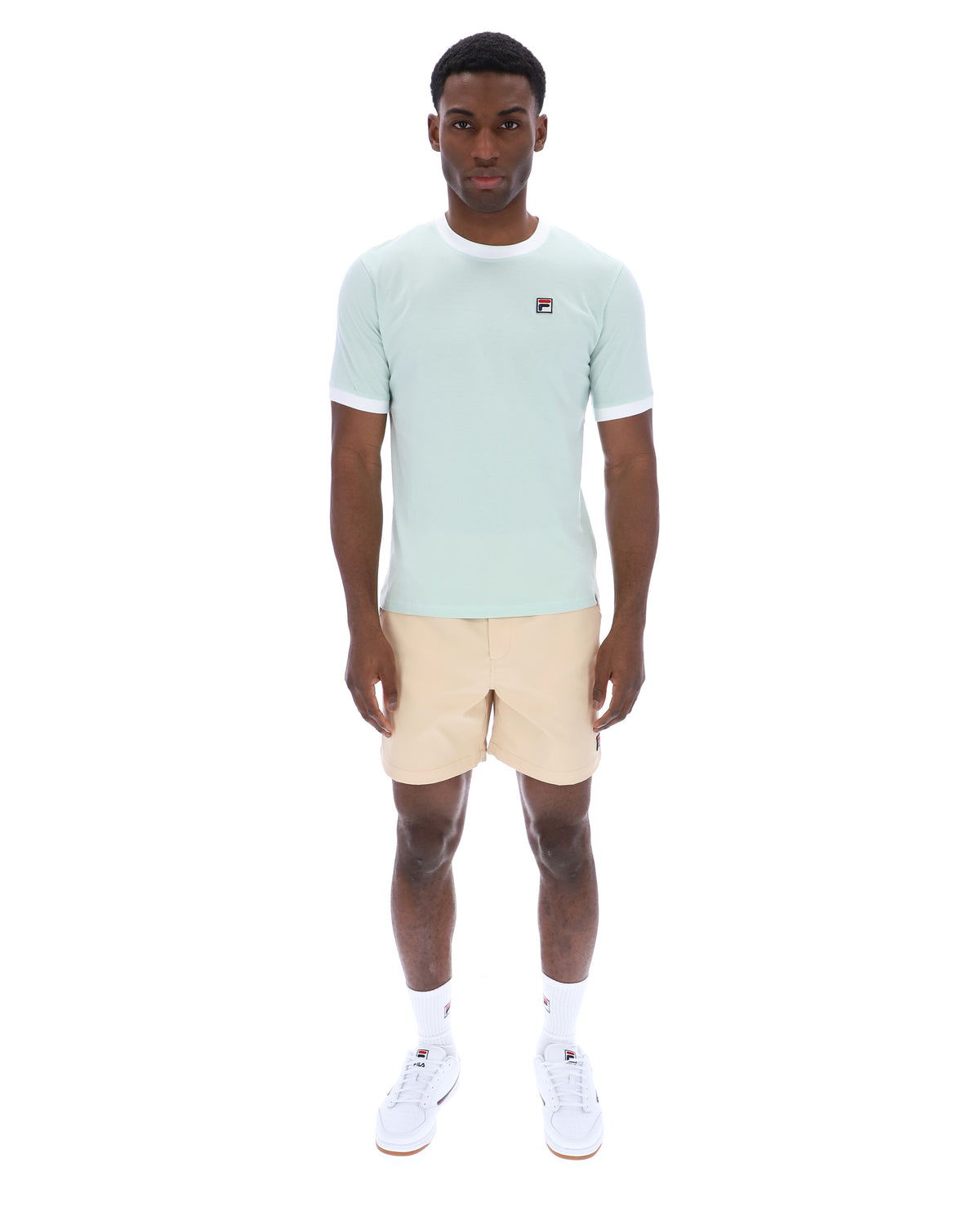 Man wearing a light green t-shirt and beige shorts on a white background