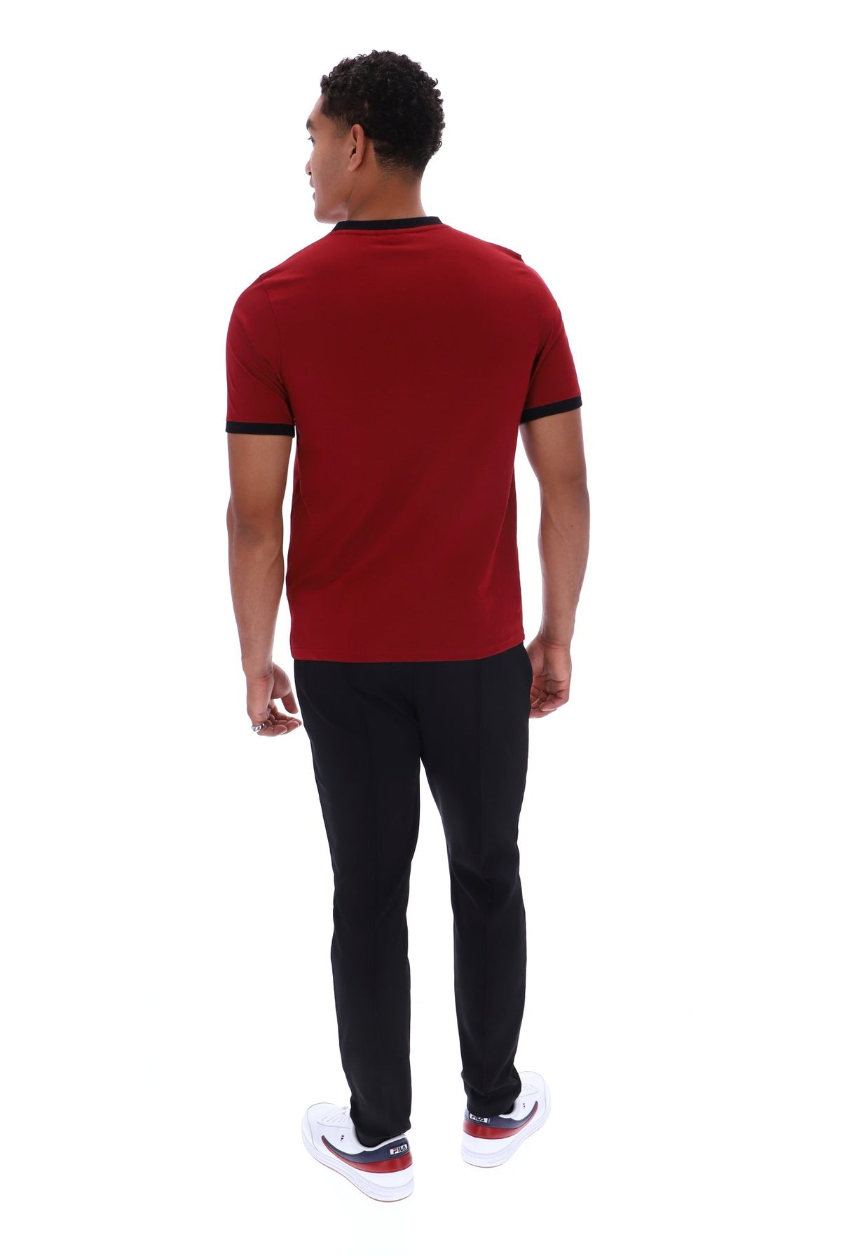 A man viewed from the back wearing a red short-sleeve t-shirt with black trim, black pants, and white sneakers, set against a plain white background.