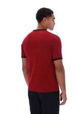 A man shown from the back wearing a red short-sleeve ringer t-shirt with black trim on the collar and sleeve cuffs, paired with black pants, against a plain white background.