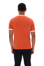 A man viewed from the back wearing a bright orange short-sleeve ringer T-shirt with white trim at the collar and sleeve cuffs, paired with black pants, against a plain white background.