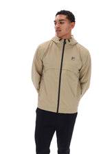 A man wearing a beige hooded windbreaker jacket with a black front zipper and a small Fila logo patch on the left chest, paired with black pants, photographed against a plain white background.