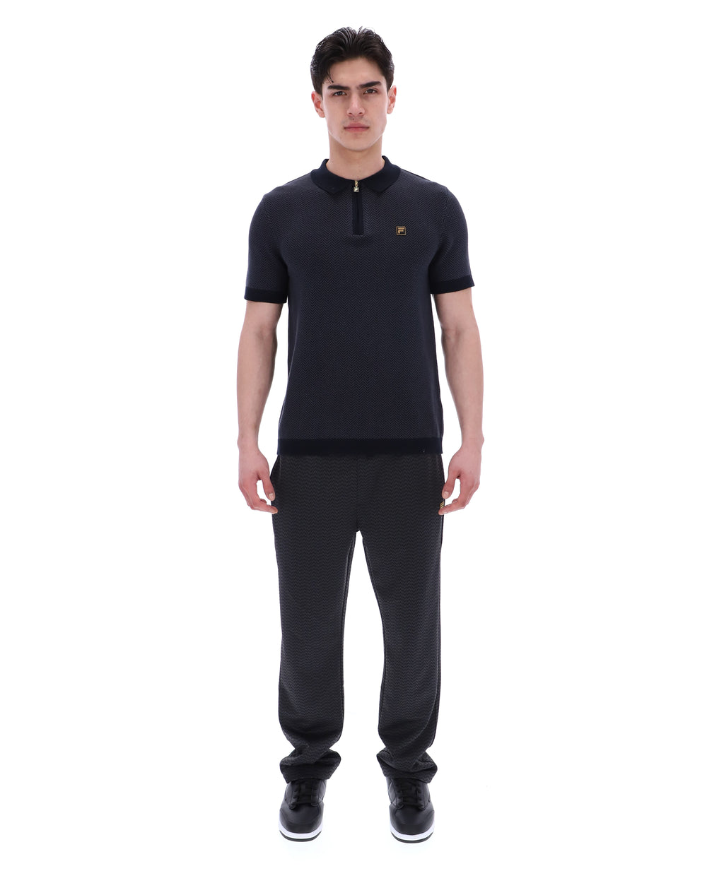 Man wearing a black outfit with a small logo on a white background
