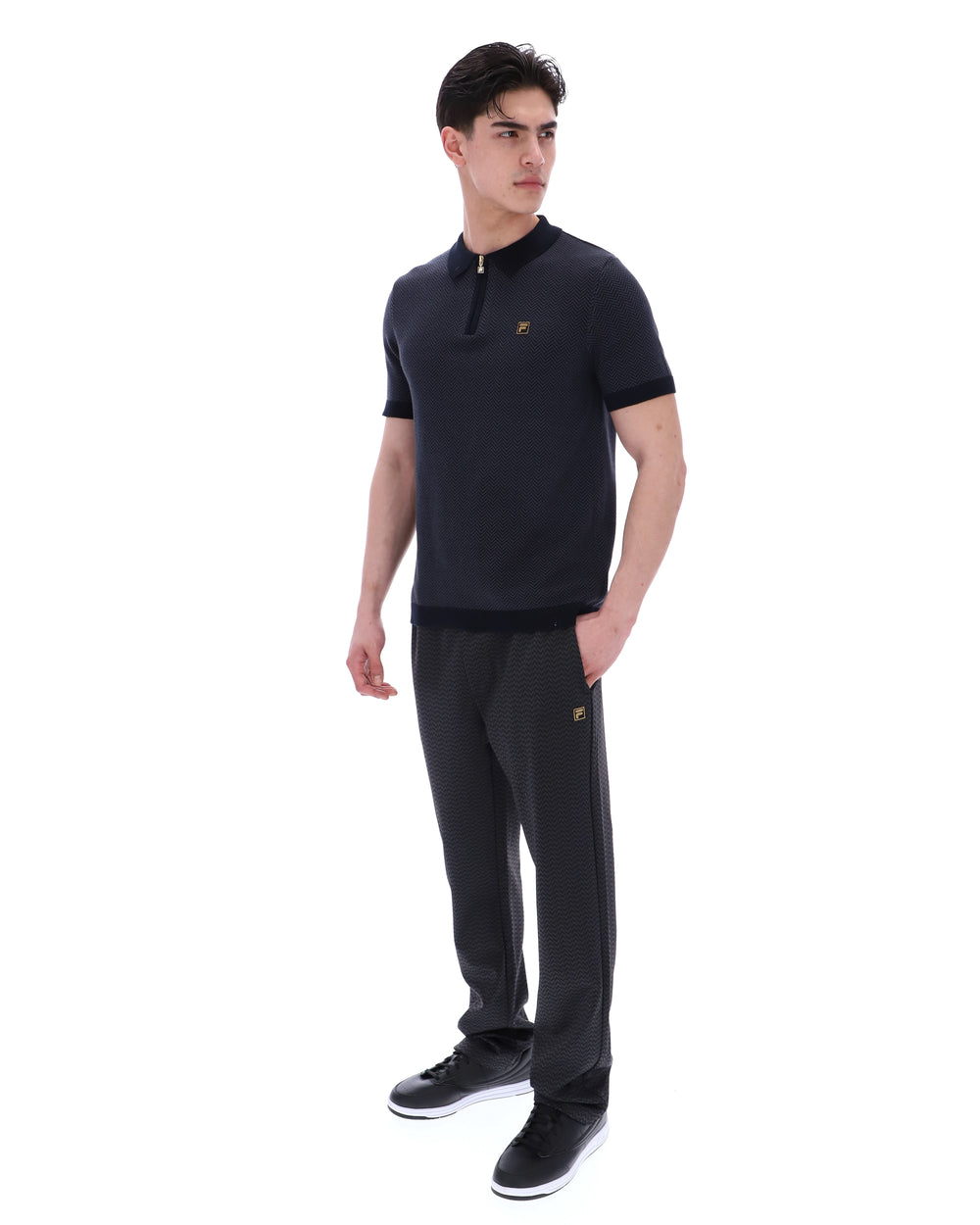 Man wearing a black polo shirt and pants with a logo on a white background