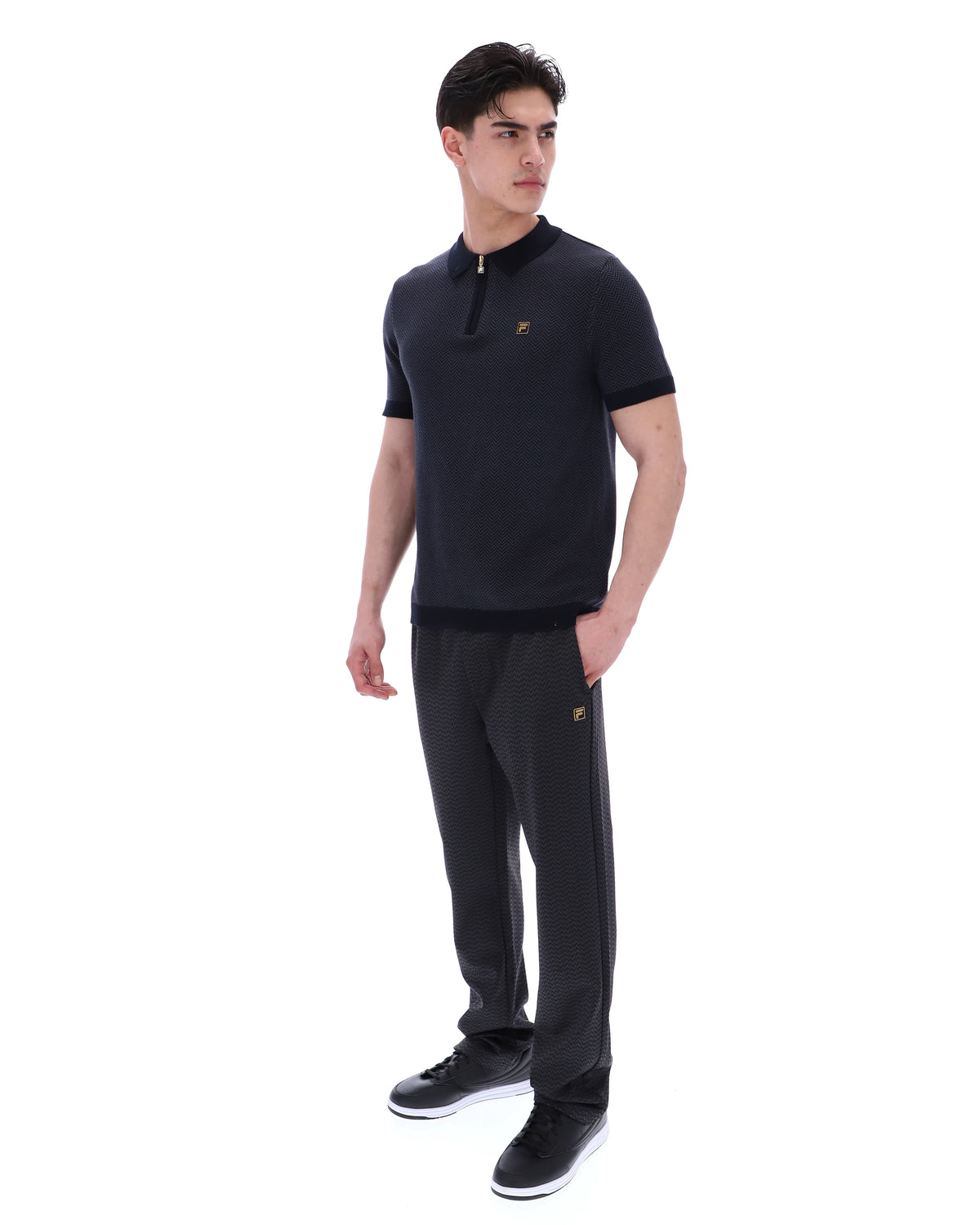 Man wearing a black polo shirt and pants with a logo on a white background