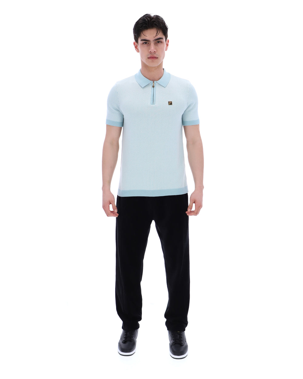 Man wearing a light blue polo shirt and black pants on a white background