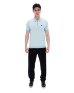 Man wearing a light blue polo shirt and black pants on a white background