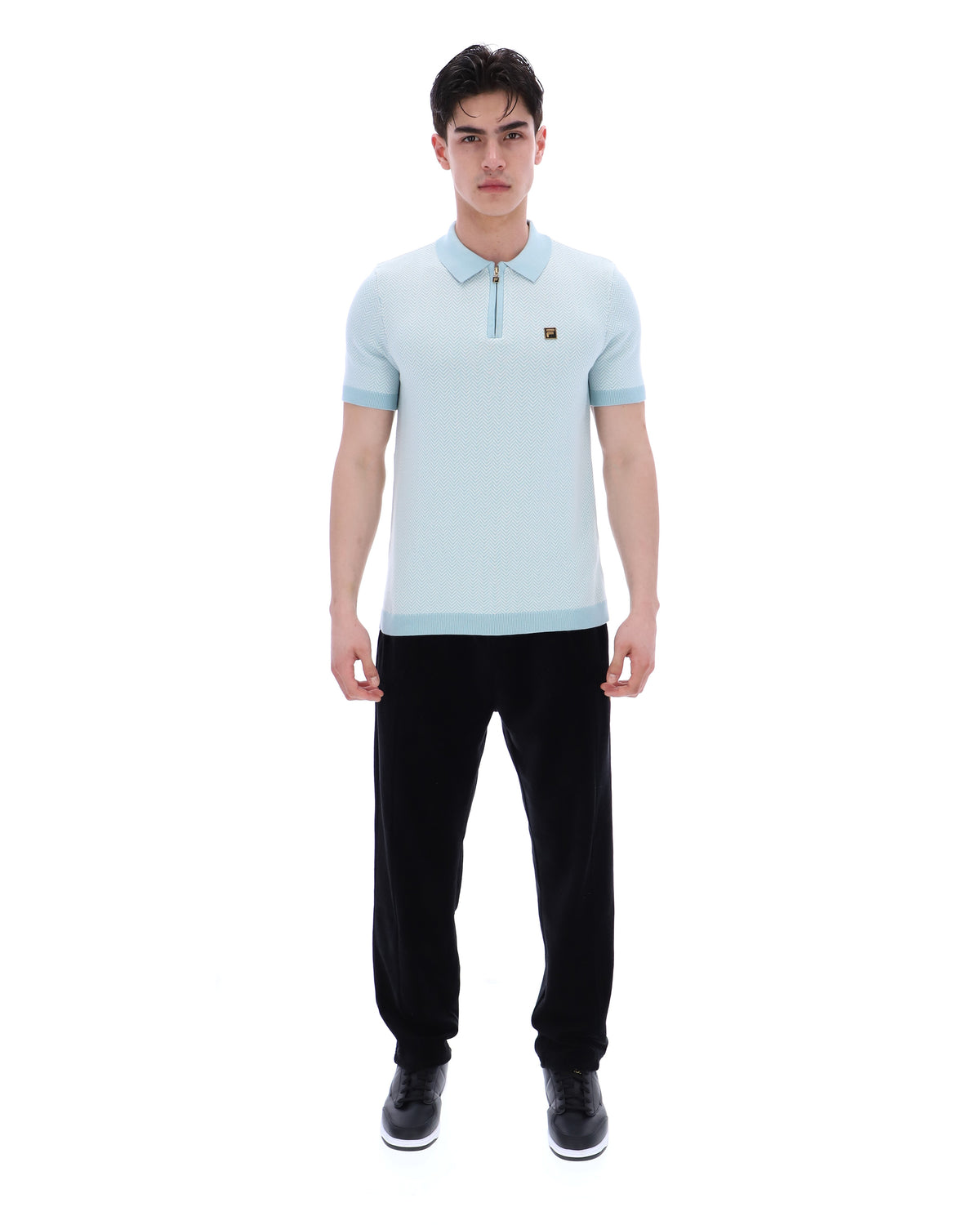 Man wearing a light blue polo shirt and black pants on a white background