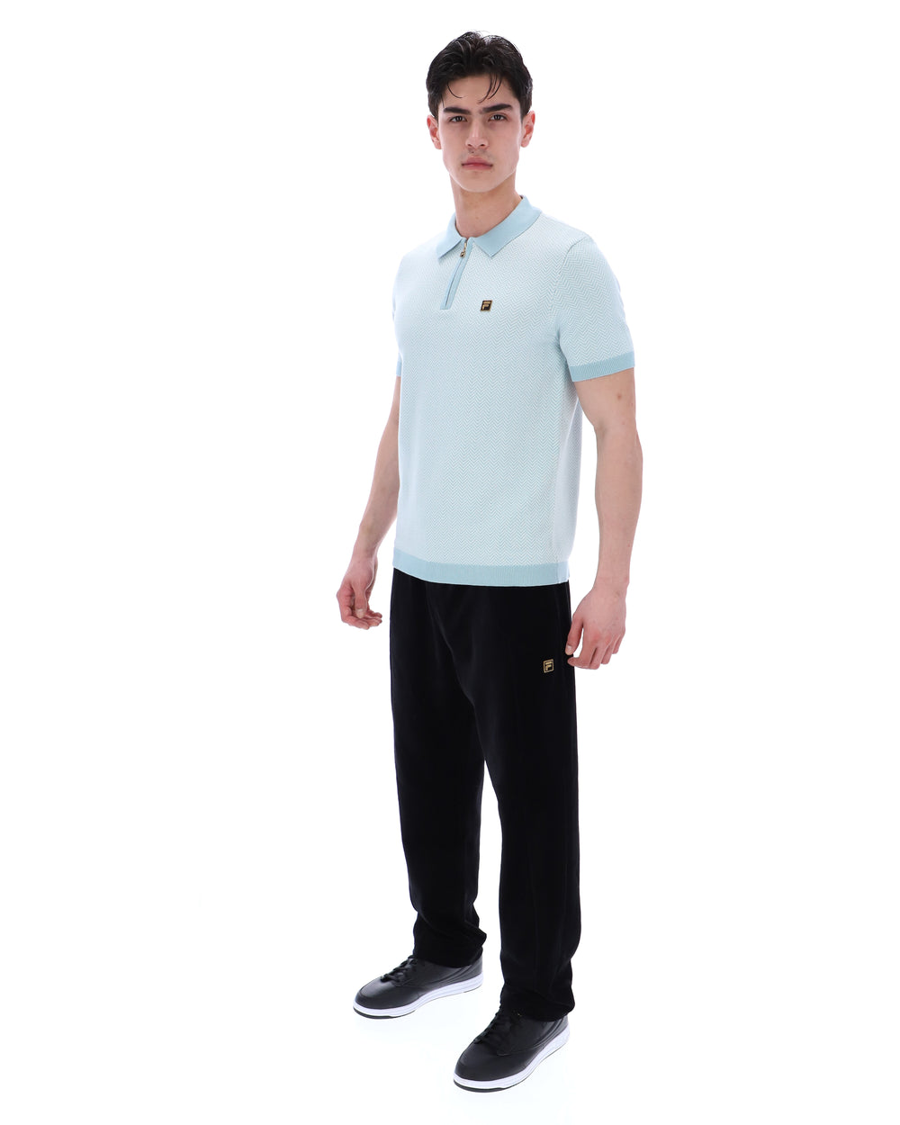 Man wearing a light blue polo shirt and black pants on a white background