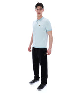 Man wearing a light blue polo shirt and black pants on a white background