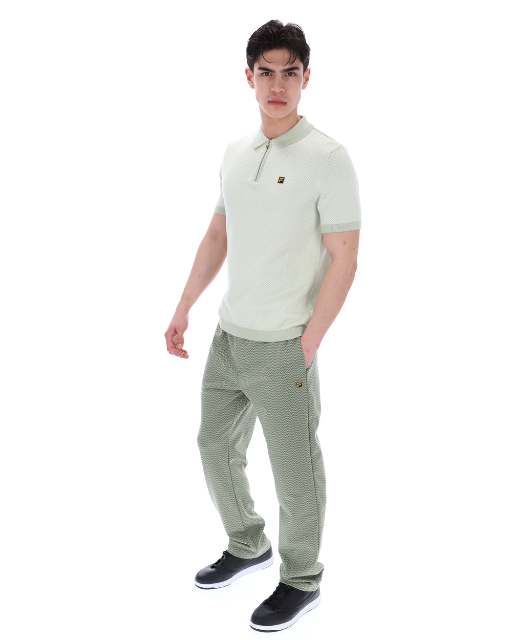 Man wearing a light green polo shirt and striped pants on a white background