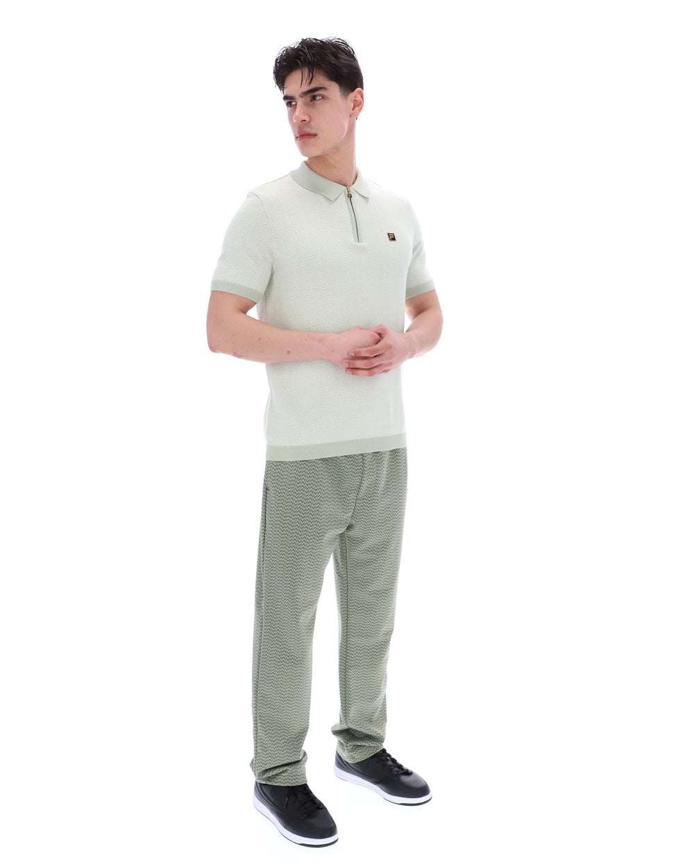 Man wearing a light green polo shirt and striped pants on a white background